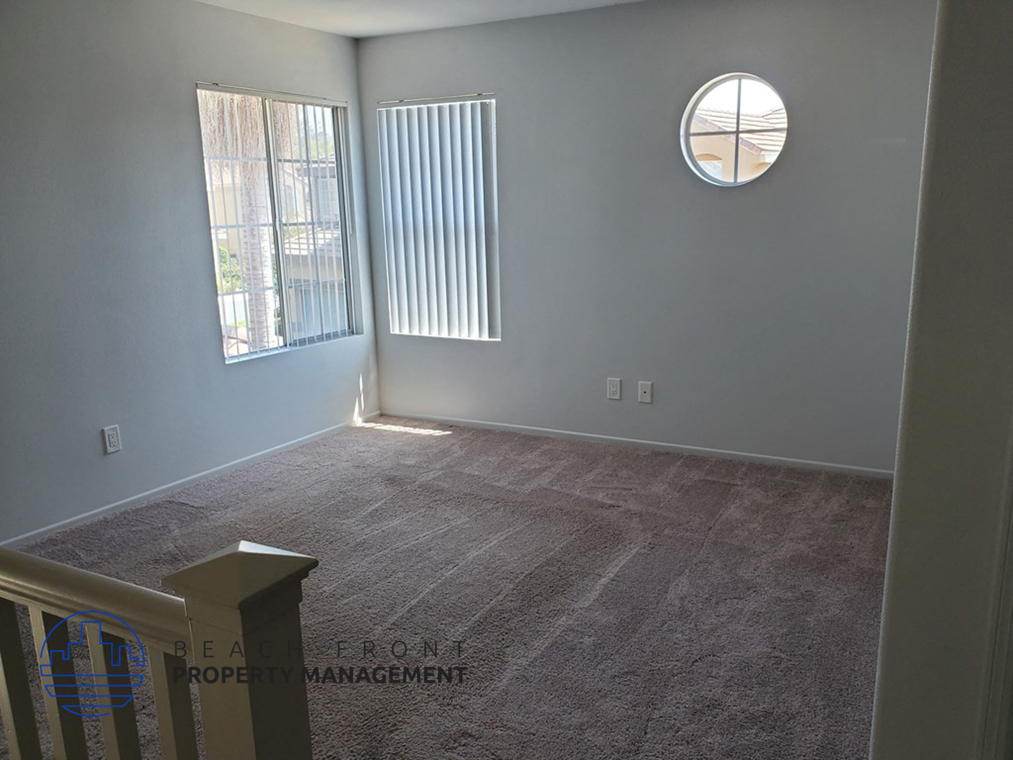 A room with a carpeted floor, a window with blinds, and a round window.